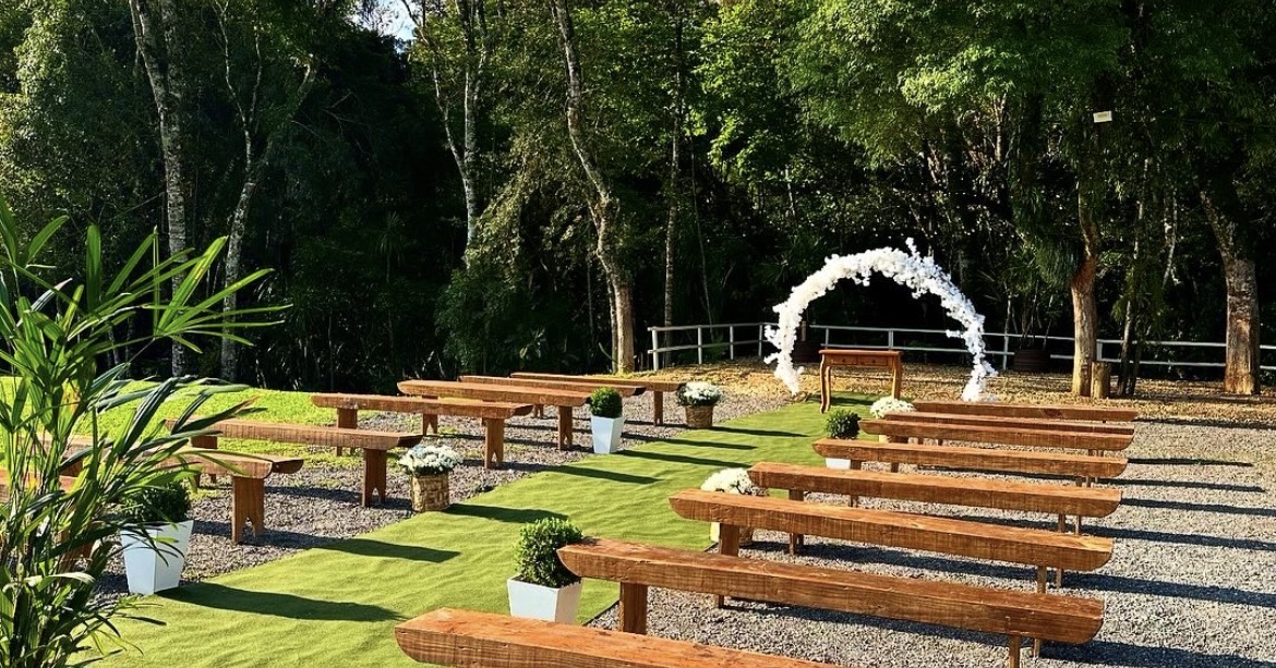 Área de cerimônia com bancos de madeira e arco floral branco